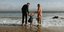 Πατέρας και μητέρα κρατούν την κόρη τους από τα χέρια στην παραλία