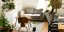 Σαλόνι διαμερίσματος με γκρι καναπέ, ξύλινες καρέκλες, βιβλιοθήκη και φυτά 