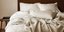 Ενα ξύλινο κρεβάτι με λευκά σεντόνια και ριχτάρι