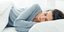 Μελαχρινή γυναίκα κοιμάται με γκρι πιτζάμες σε λευκά σεντόνια