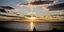 Ανθρώπινη φιγούρα πλάι στη θάλασσα παρακολουθεί το ηλιοβασίλεμα σε ένα συννεφιασμένο ουρανό