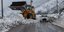 Αυτοκίνητο περνά από χιονισμένο δρόμο, δίπλα σε εκσκαφέα 