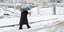 Άνδρας περπατά σε χιονισμένο δρόμο κρατώντας την ομπρέλα του