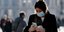 Γυναίκα με μάσκα στο Μιλάνο κοιτάζει το κινητό της
