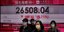 Πολίτες του Χονγκ Κονγκ με μάσκες, μπροστά σε δείκτη χρηματιστηρίου