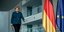 Η Ανγκελα Μέρκελ περπατά δίπλα από σημαίες Γερμανίας και ΕΕ