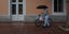 Ηλικιωμένος με ομπρέλα κουβαλάει ποδήλατο και τσάντες