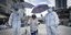 Εργαζόμενοι στη Μαλαισία με στολές και μάσκα, κρατούν ομπρέλες πάνω από ηλικιωμένη που μόλις υποβλήθηκε σε τεστ για τον κορωνοϊό