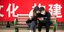Ζευγάρι στη Κίνα με μάσκες για τον κορωνοϊό κάθεται σε παγκάκι κοιτάζοντας το κινητό