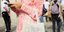 Γυναίκα με ροζ ολόσωμο σορτς και λευκή τσάντα κρατάει κινητό στα χέρια της 