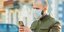 Ενας άνδρας που φορά μάσκα για τον κορωνοϊο πληκτρολογεί στο κινητό του τηλέφωνο