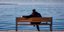 Άνδρας κάθεται σε παγκάκι με θέα την θάλασσα