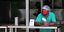Υπάλληλος στην Βραζιλία στέκεται σε τραπέζι φορώντας μάσκα για τον κορωνοϊό