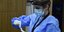 Γυναίκα με στολή, μάσκα, ασπίδα και γάντια πραγματοποιεί τεστ κορωνοϊού