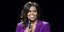 Η Μισέλ Ομπάμα με μοβ σακάκι κρατά μικρόφωνο