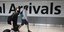 Ταξιδιώτες με βαλίτσες φορούν μάσκα για τον κορωνοϊό