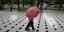 Γυναίκα περπατά κρατώντας ομπρέλα σε πλακόστρωτο 
