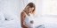 Έγκυος γυναίκα στο κρεβάτι του σπιτιού της κρατάει την φουσκωμένη κοιλιά της