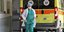 Μια νοσηλεύτρια με μάσκα τρέχει μπροστά από ασθενοφόρο