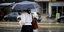 Γυναίκα περπατά στη βροχή κρατώντας ομπρέλα και καφέ