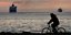Ενας ποδηλάτης μπροστά στη θάλασσα με φόντο δυο πλοία