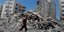 Παλαιστίνιος περπατάει πάνω στα ερείπια που άφησε ο βομβαρδισμός ενός κτιρίου από Ισραηλινούς στη Λωρίδα της Γάζας