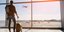 άνδρας με βαλίτσα κοντά σε τζάμι σε αεροδρόμιο με αεροπλάνο να πετάει