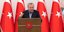 Ο Ρετζέπ Ταγίπ Ερντογάν μιλάει χτυπώντας το χέρι στο βήμα με φόντο τουρκικές σημαίες