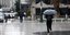 Γυναίκα με ομπρέλα περπατάει σε πλατεία υπό βροχή