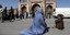 Γυναίκα με μπούργκα και παιδάκι καθιστοί στο έδαφος σε πλατεία στο Αφγανιστάν 