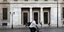 άνδρας με ποδήλατο μπροστά από κτίριο Τράπεζα της Ελλάδος