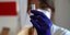 φιαλίδιο από εμβόλιο COVID σε χέρια νοσηλεύτριας με μωβ γάντια