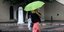 γυναίκα με πράσινη ομπρέλα περπατάει σε δρόμο ενώ έχει βροχή