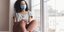 Γυναίκα με μάσκα χαζεύει παράθυρο lockdown