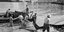 Μύκονος, 1955. Ξημερώματα στον μόλο Καμπάνη, ψαράδες ξεφορτώνουν τα δίχτυα τους για στέγνωμα και επισκευή. Το νεόκτιστο ξενοδοχείο Λητώ διαφαίνεται στο βάθος