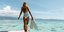 Γυναίκα με ολόσωμο λευκό μαγιό σε παραλία κρατάει βατραχοπέδιλα