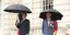 Εμανουέλ Μακρόν και βασιλιάς Κάρολος στέκονται με ομπρέλες