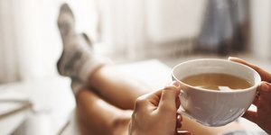Μια γυναίκα χαλαρώνει στον καναπέ της πίνοντας ένα ρόφημα