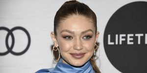 Η Τζίτζι Χαντίντ με γαλάζιο ρούχο, χαμογελάει στον φακό