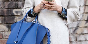 Γυναικεία χέρια κρατούν κινητό και μια μπλε τσάντα.