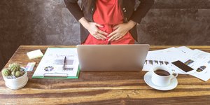 Μια γυναίκα πιάνει την κοιλιά της καθώς κάθεται στο γραφείο της