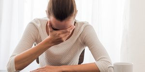 Γυναίκα με μπεζ μπλούζα πιάνει το κεφάλι της επειδή έχει πονοκέφαλο