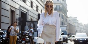 Γυναίκα με φούστα και πουκάμισο κρατάει τσάντα και περπατά στον δρόμο