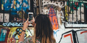 H πλάτη μιας γυναίκας που φωτογραφίζει με το κινητό της γκράφιτι