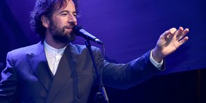 O Kωστής Μαραβέγιας με κοστούμι σε συναυλία μπροστά από το μικρόφωνο