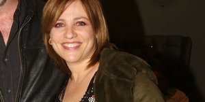 Η Μαριάννα Τουμασάτου με φόρεμα και πράσινο παλτό χαμογελάει