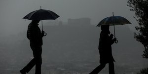 Πεζοί με ομπρέλες κάτω από τον σκοτεινό ουρανό