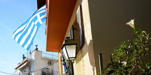 Σπίτι με σημαία πολυκατοικία στο βάθος και μια πινακίδα