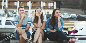 Ενα αγόρι και δύο κορίτσια κάθονται σε ένα παγκάκι και χαμογελούν