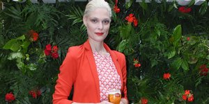 Η Αναστασία Περράκη με φόρεμα και κόκκινο σακάκι και λουλούδια στο φόντο